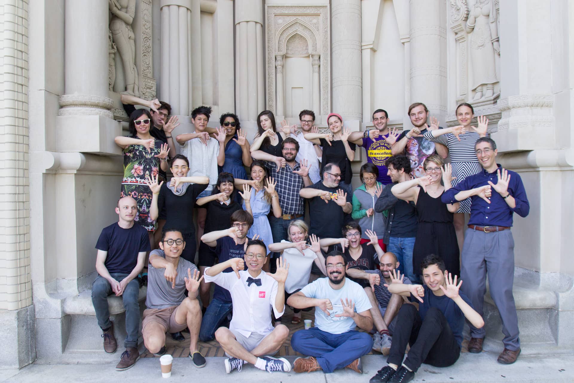 Diverse group of participants smile and make a p5 sign with their hands"