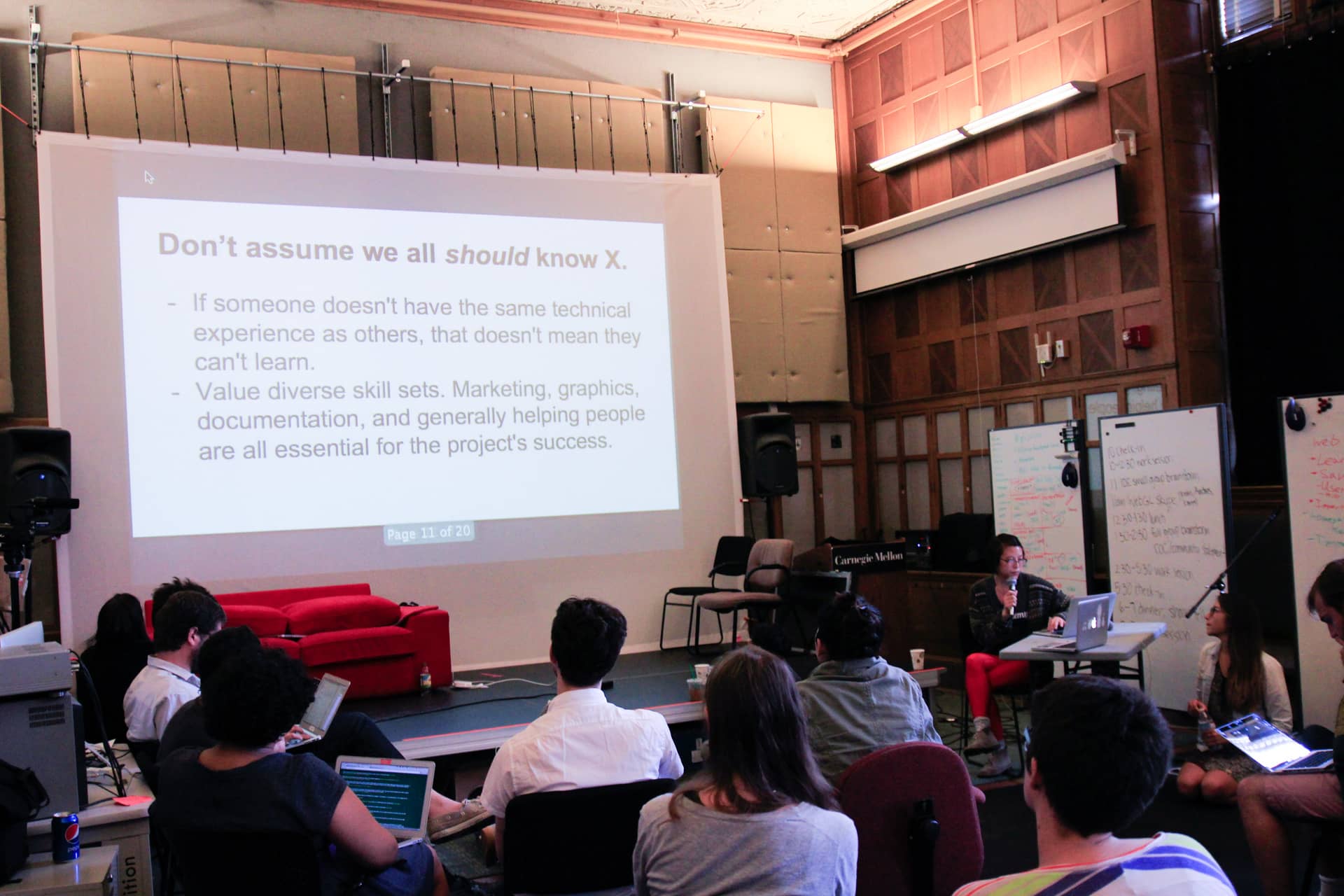 Woman speaking into a microphone about valuing different skill sets while a group of participants with laptops look at her powerpoint in a classroom"