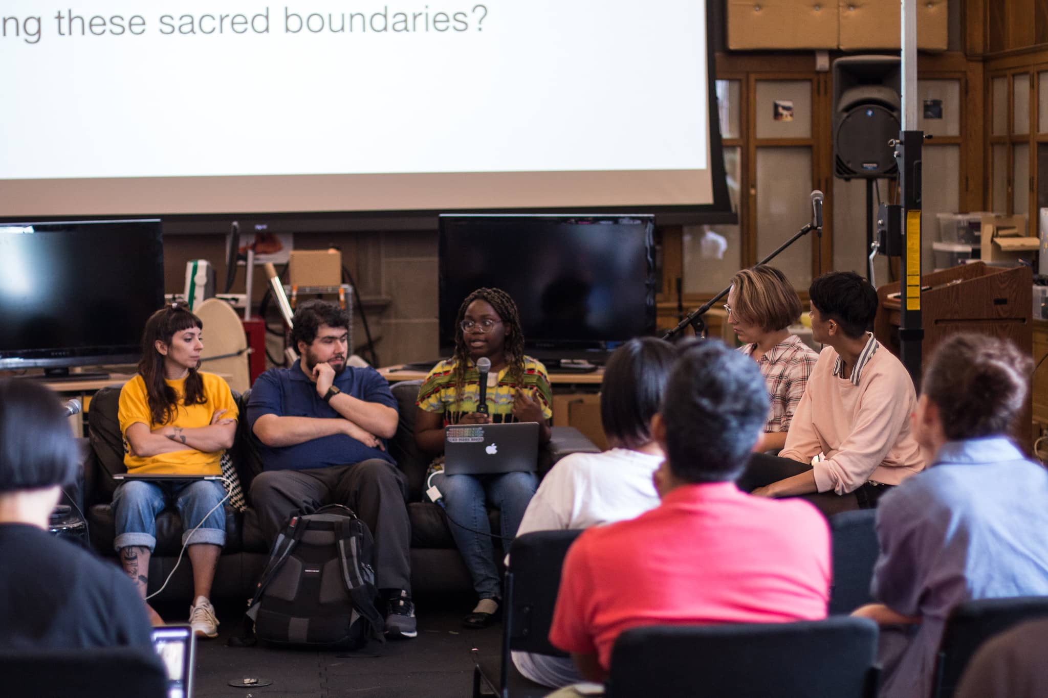 Woman with microphone speaking to fellow participants with the text sacred boundaries in the projection behind her"